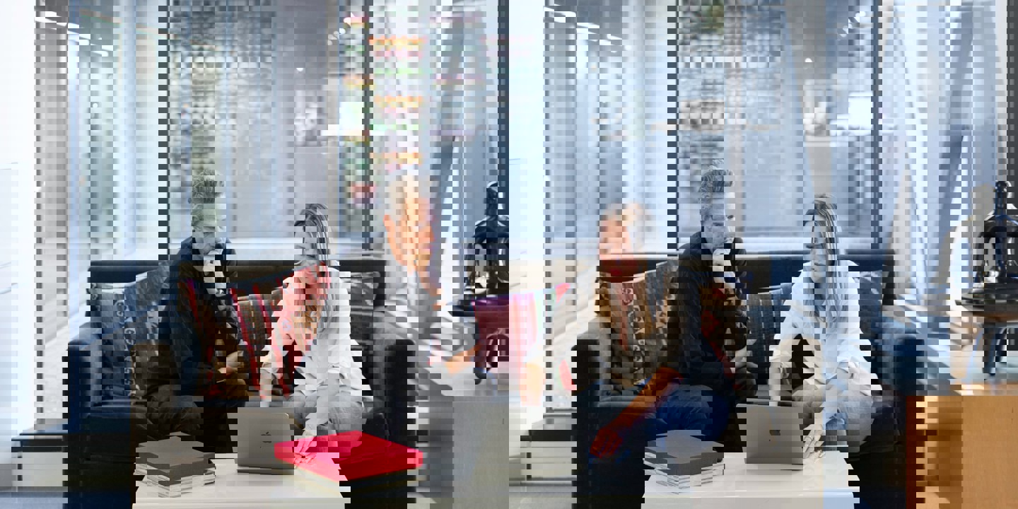 Man and women looking at laptop on sofa with glass office behind